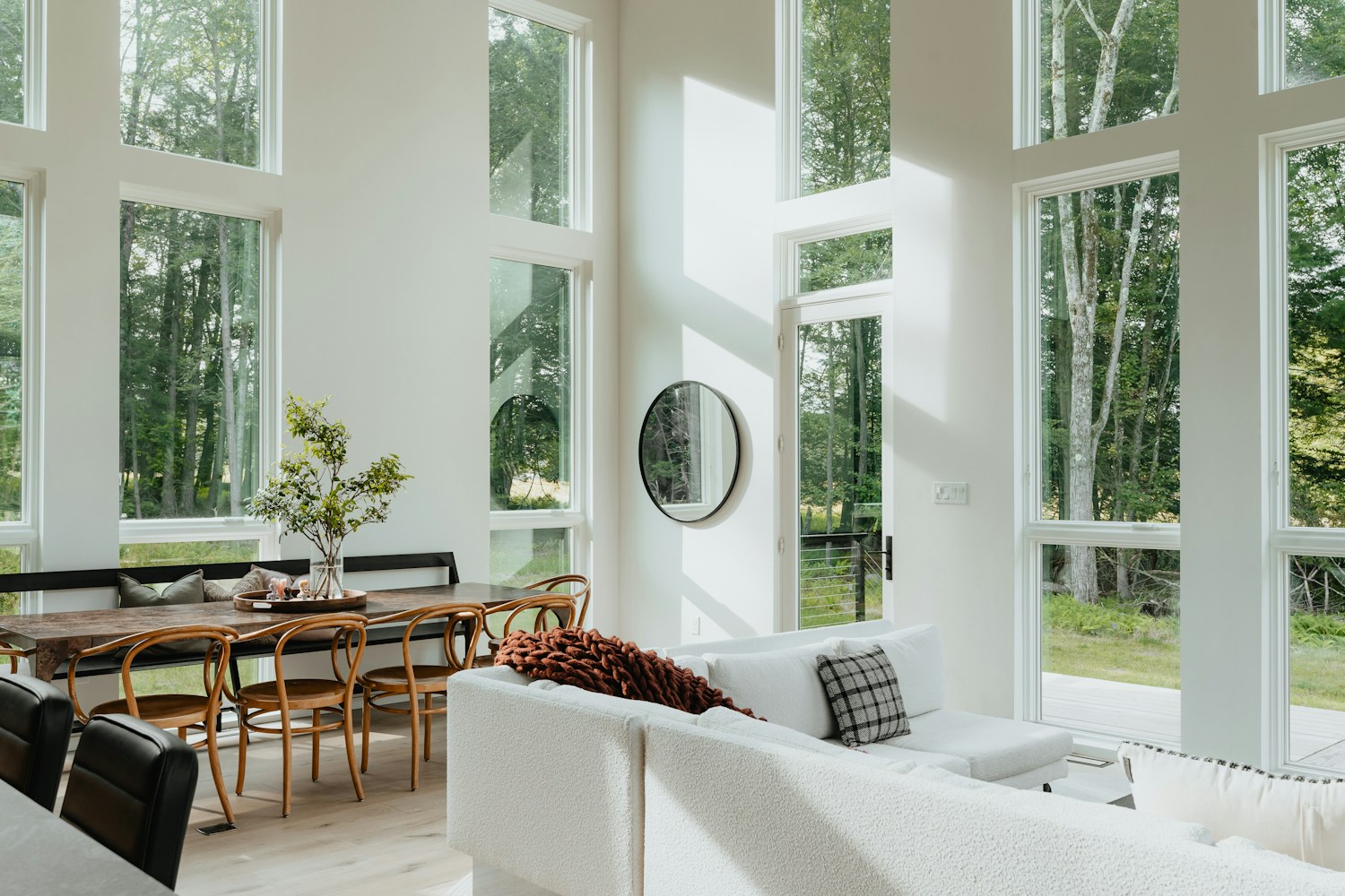 A bright living room with large white-framed windows overlooking trees
